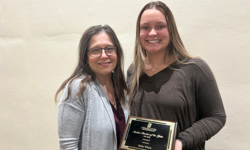  English teachers Vanessa Halling and Bailey Wilcox smile together with Wilcox holding a plaque.